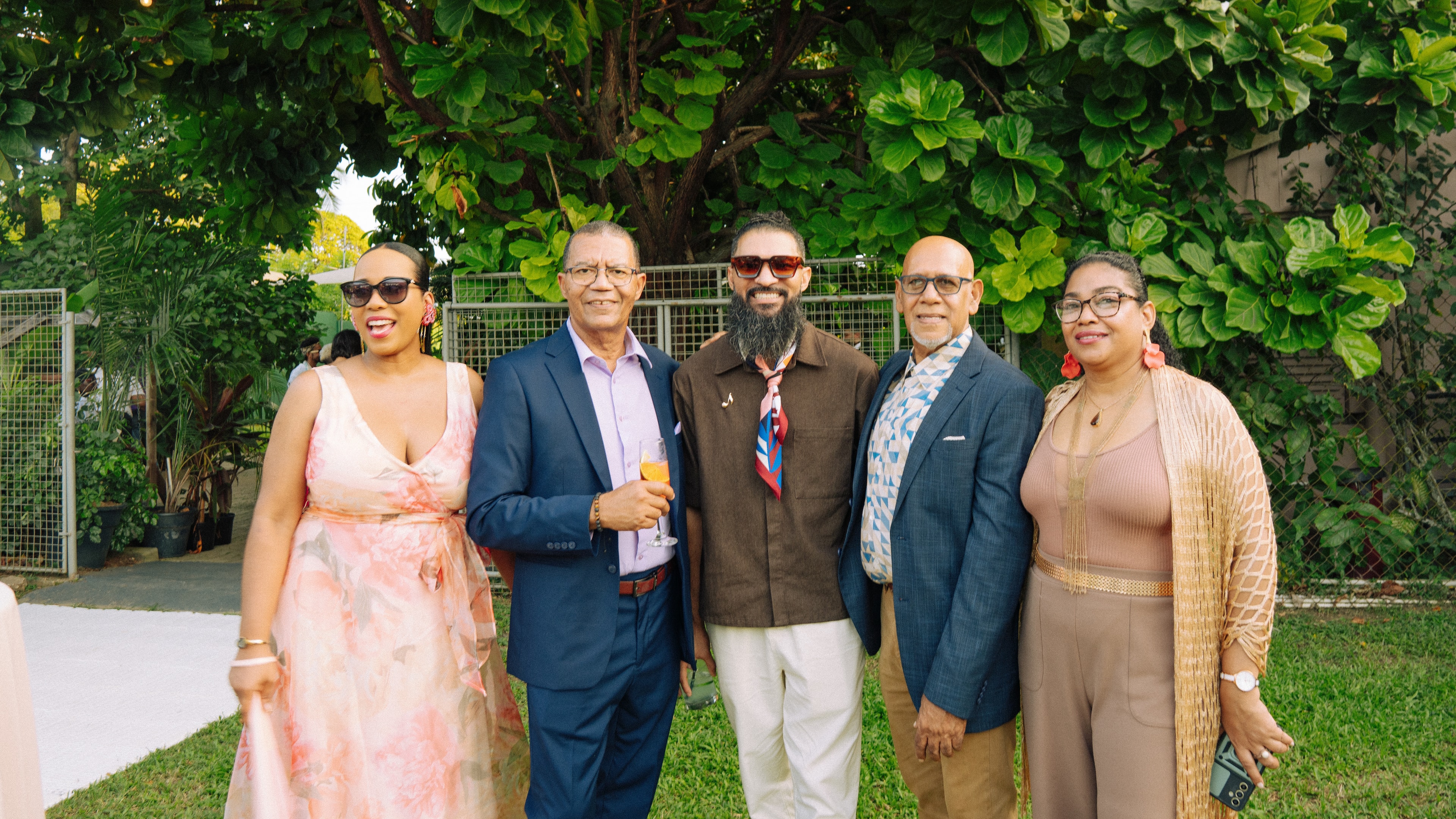 Five wedding guests posing together beneath a leafy tree