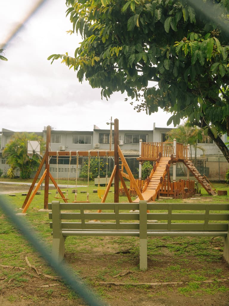 A wooden playground and green bench beneath a leafy tree